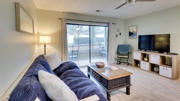 A living room with a sofa, a coffee table, a TV, and a sliding glass door leading to an outdoor area. - 5 Mi to Cherry Grove Beach: Dog-Friendly Condo! (Little River)