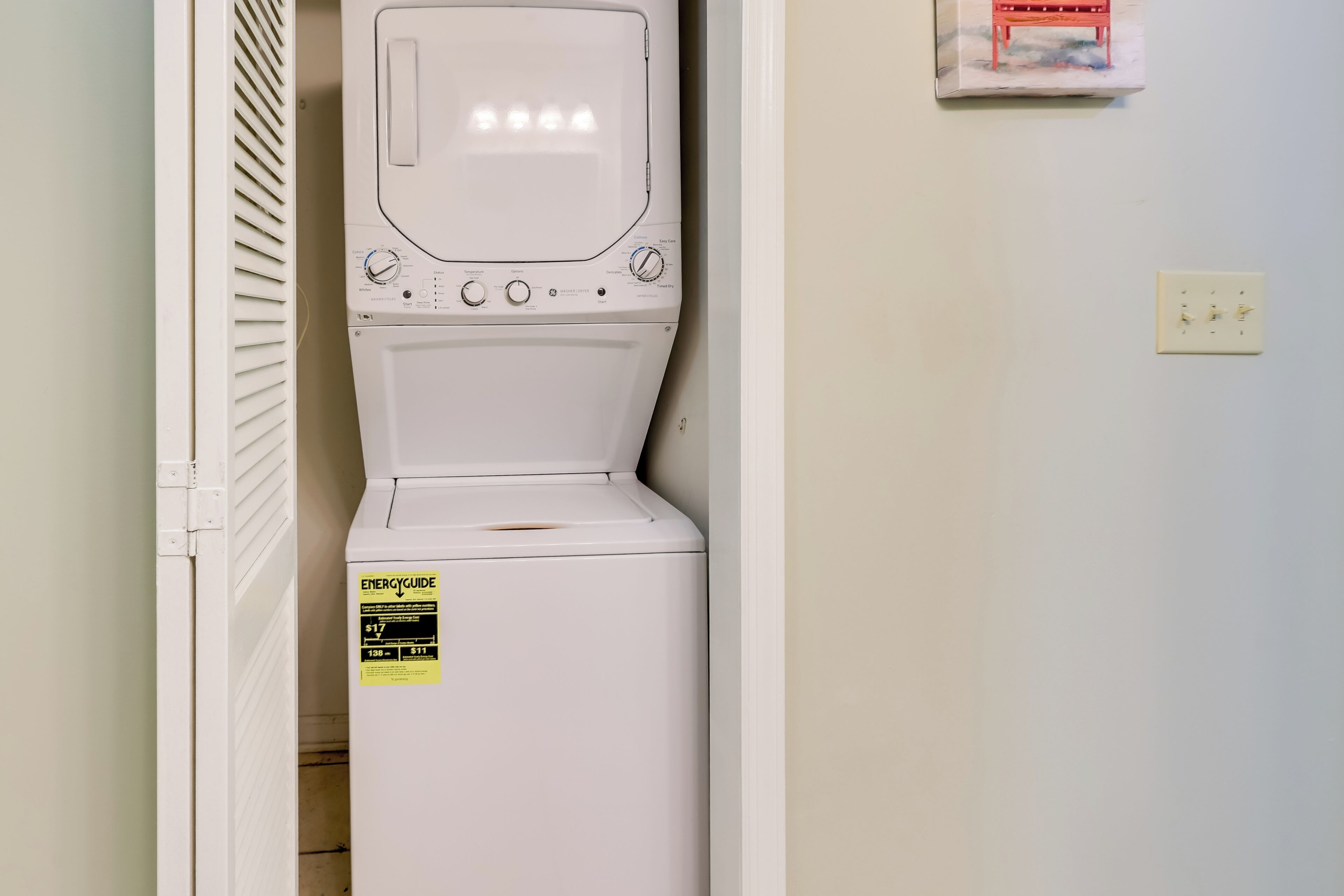 Una lavadora de carga frontal blanca con un panel de control, una etiqueta amarilla de eficiencia energética y un enchufe en la pared.