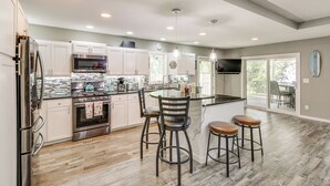 A modern kitchen with a central island, bar stools, and a dining area with a view.