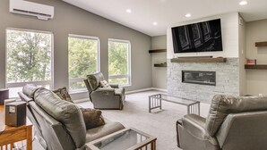A spacious living room with a fireplace, leather sofas, and a large TV mounted on the wall.