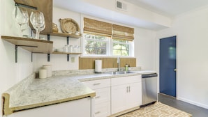 A kitchen with white cabinets, a marble countertop, wooden shelves, and a window with blinds. - Athens Apartment for Saturdays Between the Hedges (Athens)
