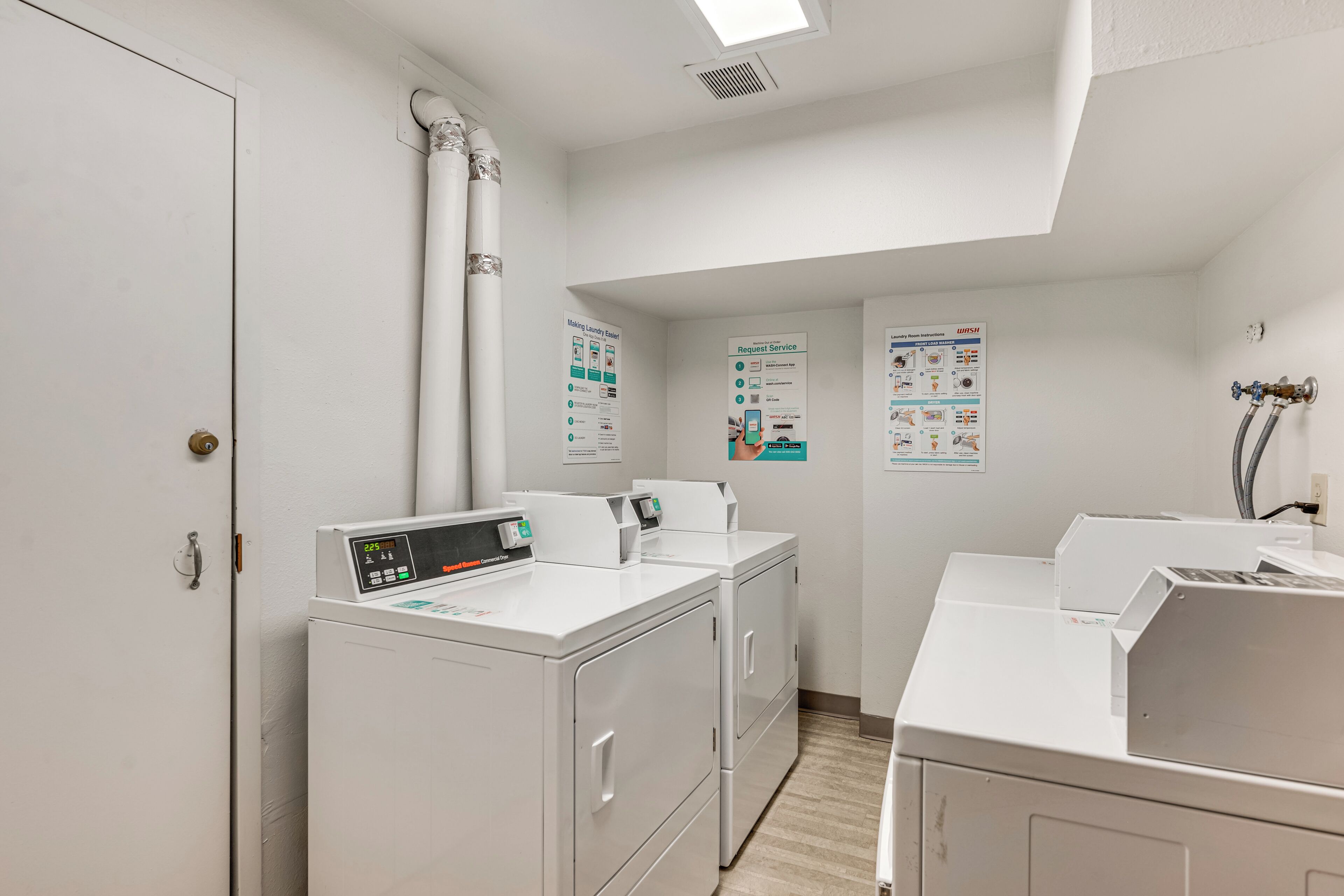 A laundry room with a front load washer, a dryer, and a wall-mounted washing machine. There are instructional posters on the wall.