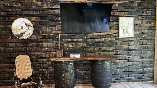 A rustic room with a wooden wall, a television mounted above a wooden table, a vintage chair, and two barrels. - 3-bedrooms, 2 bathrooms upstairs cabin in charming French Lick with AC (French Lick)
