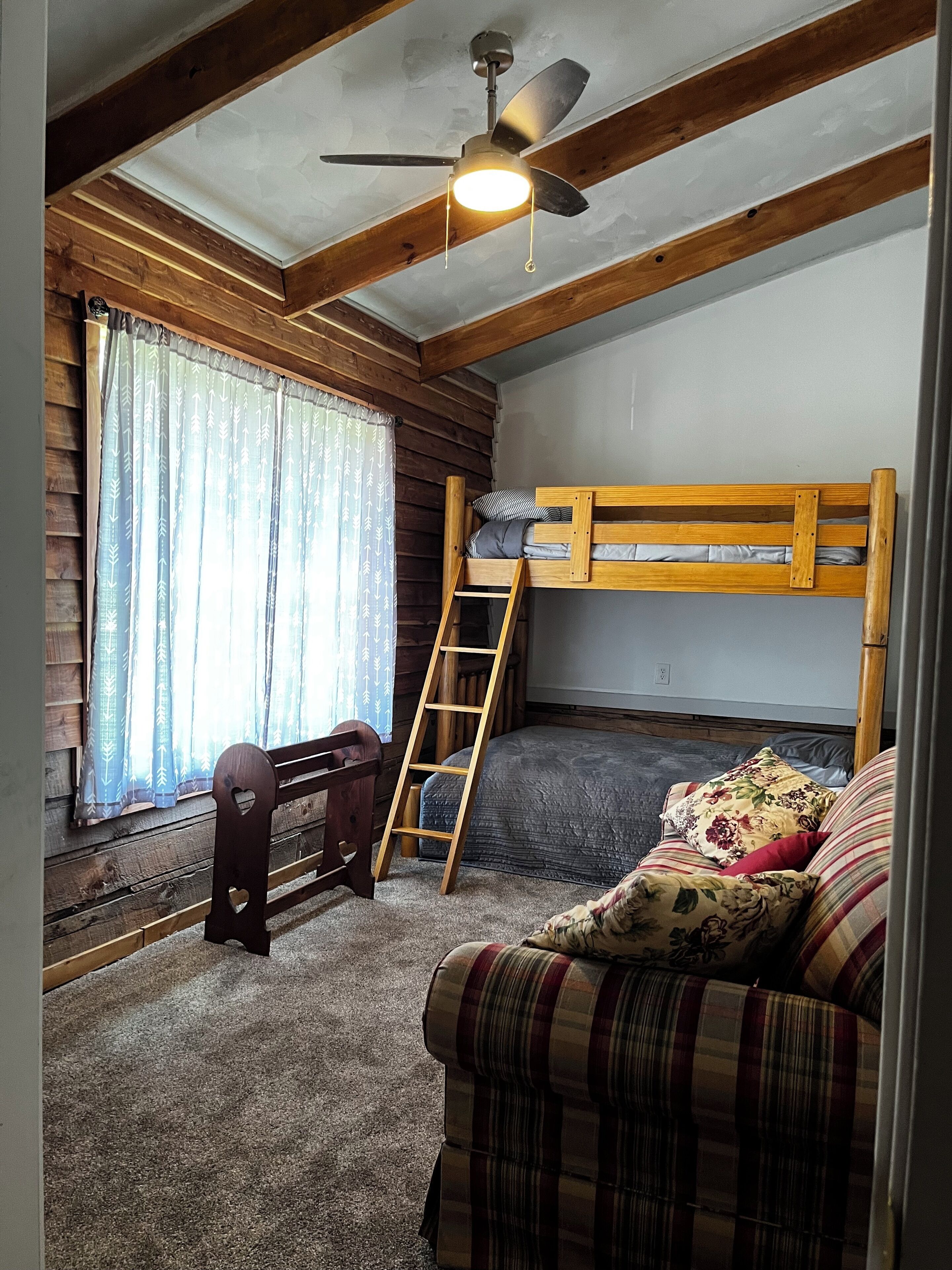 A room with a bunk bed, a desk, a chair, a ladder, and a sofa.