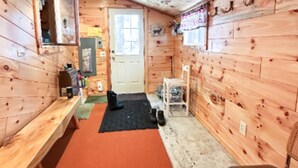 Interior de una cabaña de madera con un banco, una puerta, una silla y una pequeña alfombra.