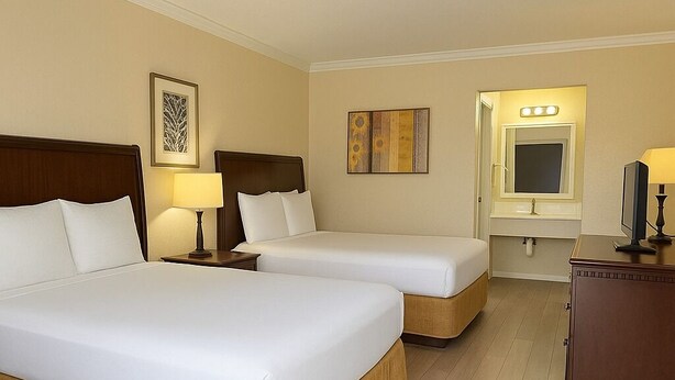 A hotel room with two beds, a vanity with a mirror, and a television on a wooden cabinet. - Unno Boutique Hotel  (Kissimmee)