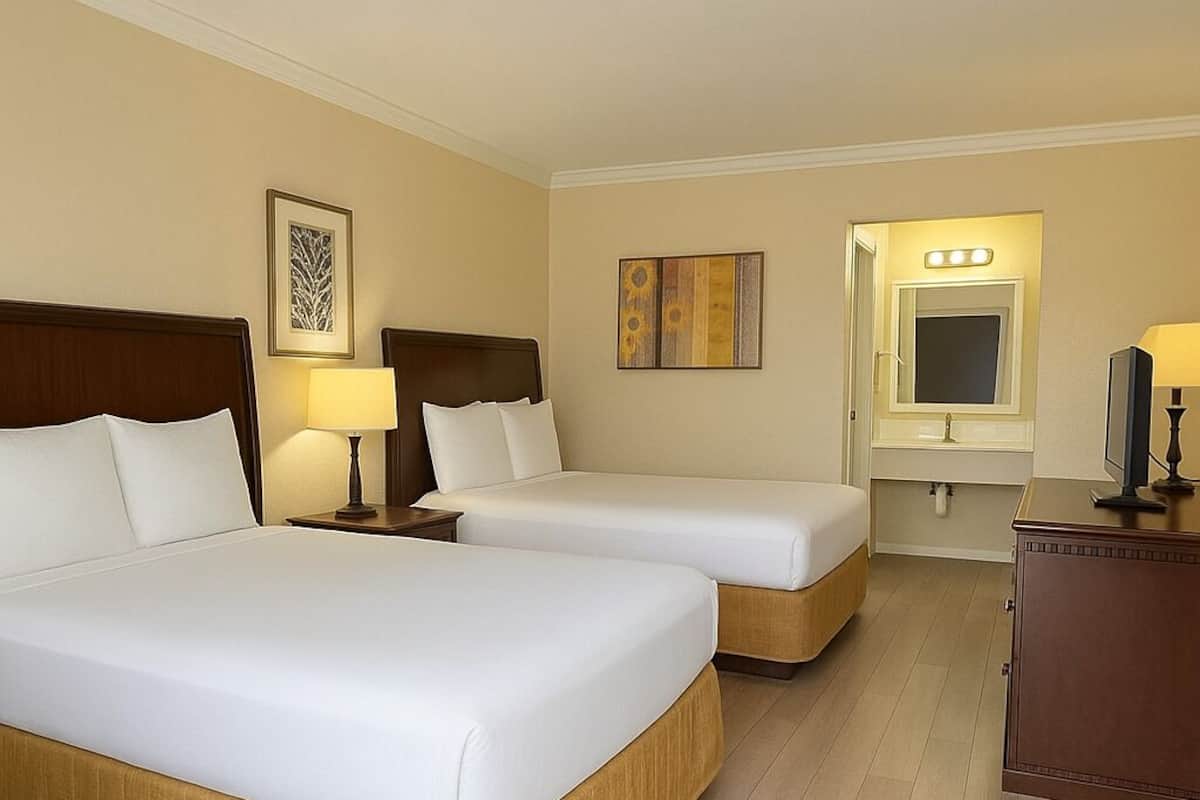 Ein Hotelzimmer mit zwei Betten, einem Schminktisch mit Spiegel und einem Fernseher auf einem Holzkasten.