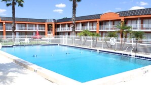 A swimming pool with a white fence, palm trees, and a building with multiple balconies in the background. - Unno Boutique Hotel  (Kissimmee)