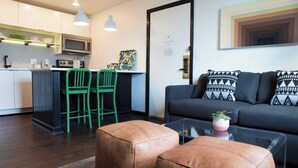 Een moderne keuken met een magnetron, groene stoelen en een eethoek. Er is een bank met gekleurde kussens en een glazen salontafel.