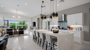 A modern kitchen with a large island, bar stools, and pendant lighting.