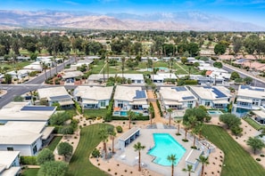 A residential area with modern houses, a central swimming pool, and a mountain backdrop. - Modern Desert Retreat | Pool, Spa, EV Charger, Near Tennis Garden (Indian Wells)