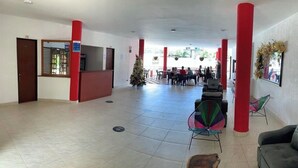 Un hall d’entrée spacieux avec des piliers rouges, un comptoir d’accueil et un guichet pour l’enregistrement.