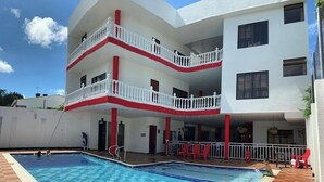 Un immeuble à plusieurs étages doté d’une piscine, de balcons et d’une façade aux couleurs rouge et blanche.