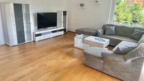 A modern living room with a flat-screen TV, grey sofa, and white coffee table.
