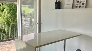 A modern kitchen with a glass countertop, a bar stool, and a shelf with bottles and framed pictures.