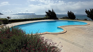 A swimming pool with a curved edge, surrounded by a paved deck and greenery. - Villa Rita Luxury resort (Golfo Aranci)