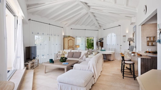 A spacious living room with a high ceiling, a television, a sofa, a coffee table, and a dining area with a kitchen counter. - Villa Rita Luxury resort (Golfo Aranci)
