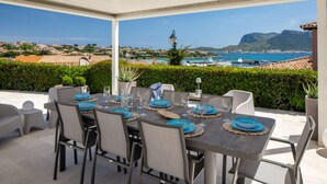 An outdoor dining area with a table set for four, overlooking a coastal landscape with boats and mountains. - Villa Rita Luxury resort (Golfo Aranci)