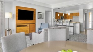 Ein modernes Hotelzimmer mit Essbereich, einer Küchenzeile und einem Flachbildfernseher, der an einer Holzvertäfelung angebracht ist.
