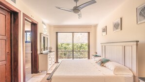 Un dormitorio con cama, cómoda, mesita de noche, ventilador de techo y balcón con vista a follaje.