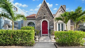 A building with a red door, stone facade, and a small porch with steps leading up to it.