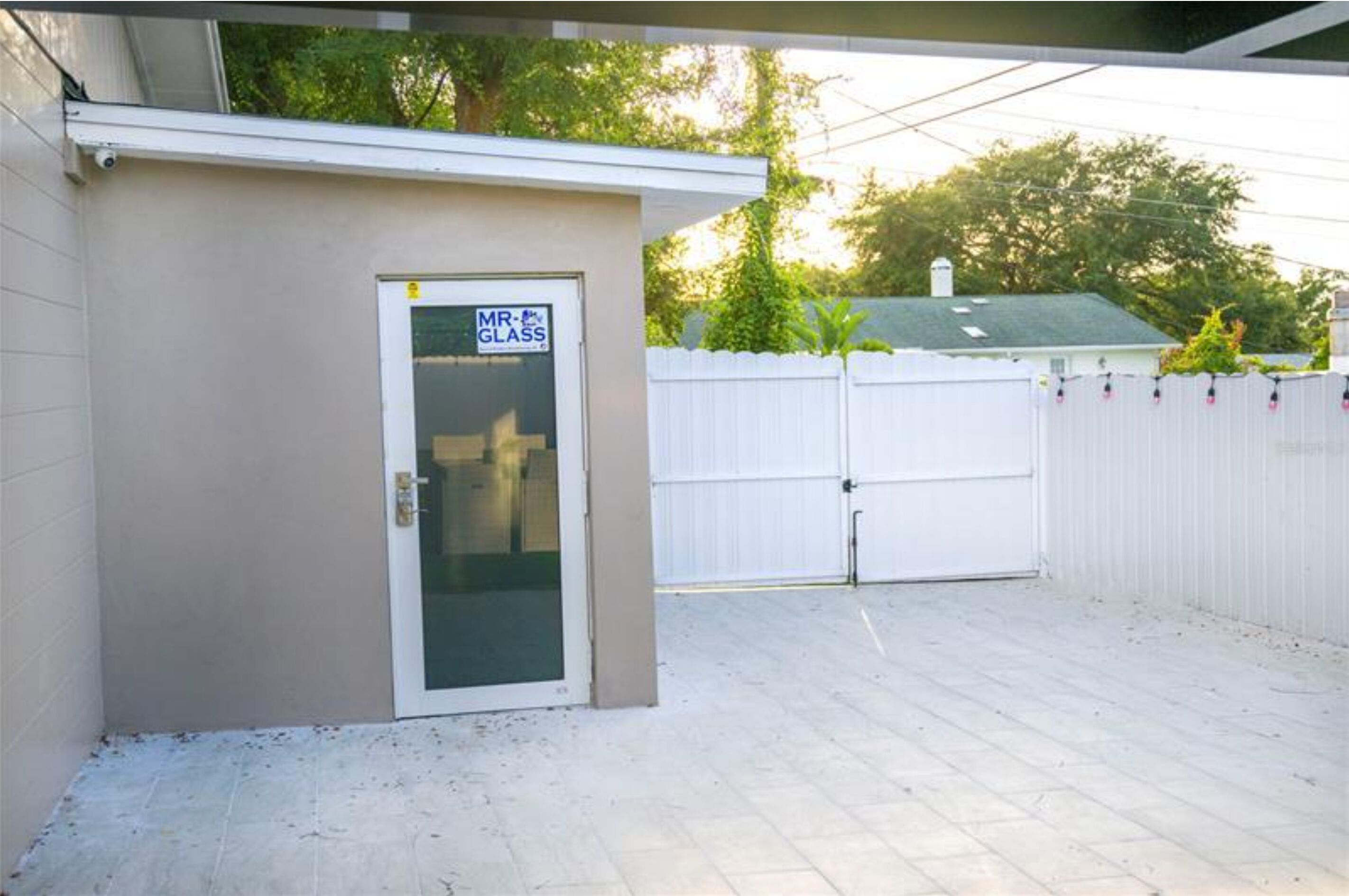 A small, single-story building with a door labeled "MR. GLASS" and a white fence in the background.