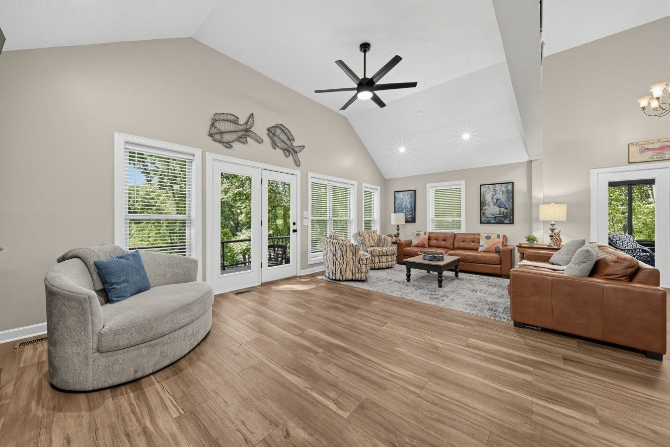 A spacious living room with a high ceiling, a ceiling fan, and a large window with blinds.