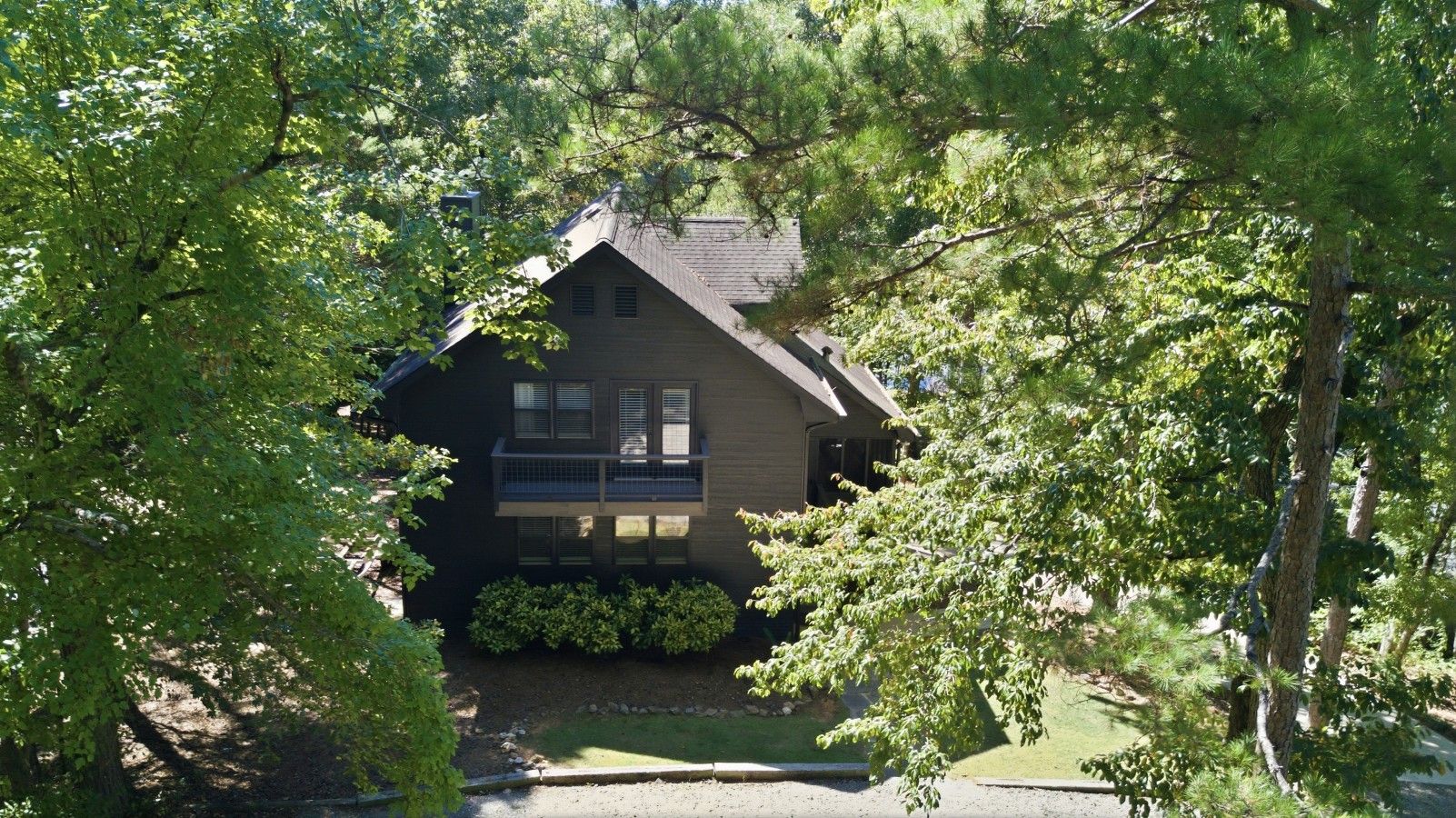 Une maison à deux étages dotée d’un balcon, entourée d’arbres et d’une pelouse bien entretenue.