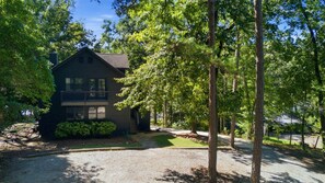 Une maison à deux étages avec un porche à l’avant, entourée d’arbres et donnant sur une allée.