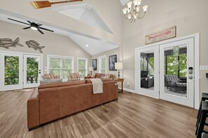 A spacious living room with a large brown sectional sofa, a ceiling fan, and a chandelier.