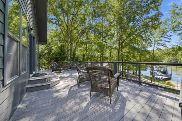 A wooden deck with outdoor furniture, overlooking a body of water and trees.