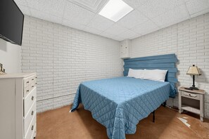Une chambre à coucher comprenant un lit, une table de chevet, une commode et un téléviseur.