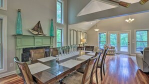 A spacious dining area with a long wooden table and chairs, a fireplace, and large windows offering views of the outdoors.