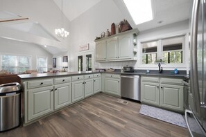 A spacious kitchen with light green cabinets, a stainless steel dishwasher, and a large island.