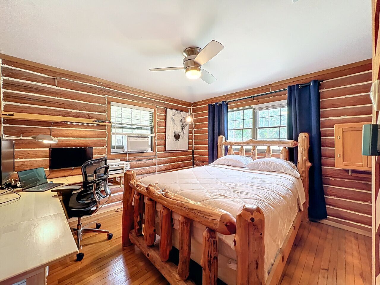 Ein Blockhauszimmer mit Bett, Schreibtisch, Stuhl und Deckenventilator.