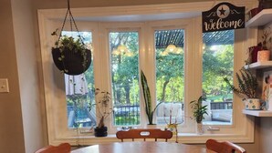 A dining area with a round wooden table and chairs, a hanging plant, and a 'Welcome' sign.