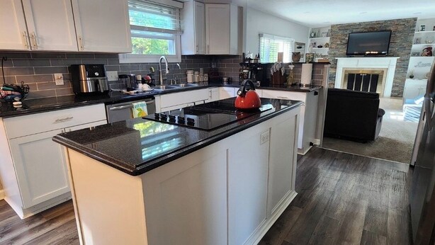 A modern kitchen with white cabinets, a large island, and a stone fireplace.