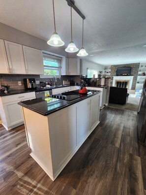 A modern kitchen with white cabinets, a large island, and a stone fireplace. - Spacious 5-bedroom house in charming Granger with Hot Tub near Notre Dame (Granger)