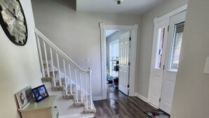 A hallway with a wooden floor, white walls, a staircase with white railings, and a ceiling light fixture.