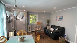 A cozy living room with a dining area, a black leather sofa, and a TV mounted on the wall. - Beautifully appointed 2 bedroom with access to a private beach! (DENNIS PORT)