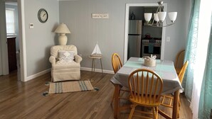 A dining area with a table set for four, a chair, a lamp, and a small side table. - Beautifully appointed 2 bedroom with access to a private beach! (DENNIS PORT)