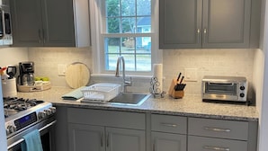 A modern kitchen with grey cabinets, a stainless steel stove, a microwave, and a toaster. - Beautifully appointed 2 bedroom with access to a private beach! (DENNIS PORT)