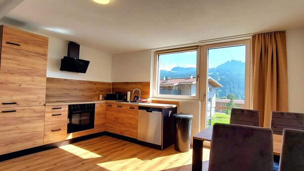 Une cuisine moderne avec des meubles en bois, un lave-vaisselle et une fenêtre donnant sur un paysage montagneux.