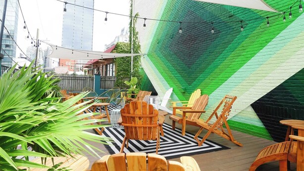 An outdoor seating area with wooden chairs and tables, a green wall mural, and string lights. - Sleeps 8 4 Stylish Sobro Suites Near Music & Dining by Avantstay (Nashville)