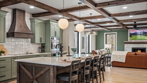 A modern kitchen with a large island, wooden beams, and pendant lighting.