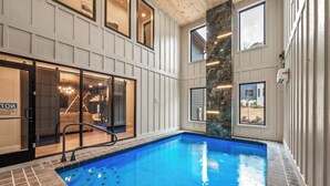 An indoor swimming pool with clear glass walls, a wooden ceiling, and a stone accent wall.