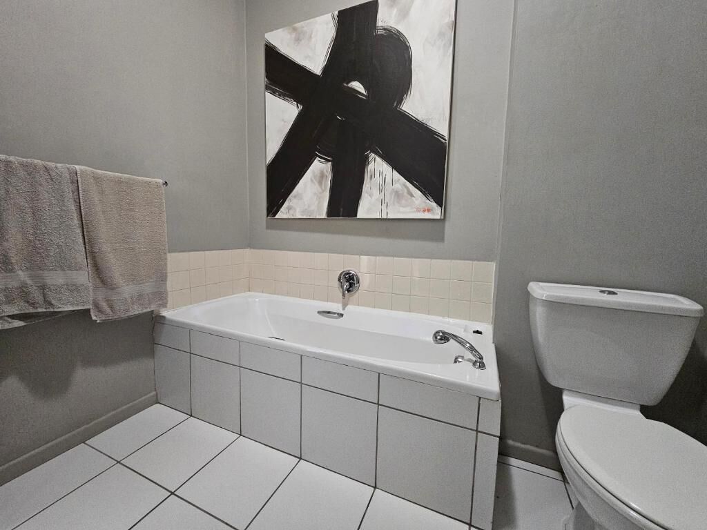 Ein Badezimmer mit Badewanne, Toilette und einem großen, abstrakten Gemälde an der Wand.