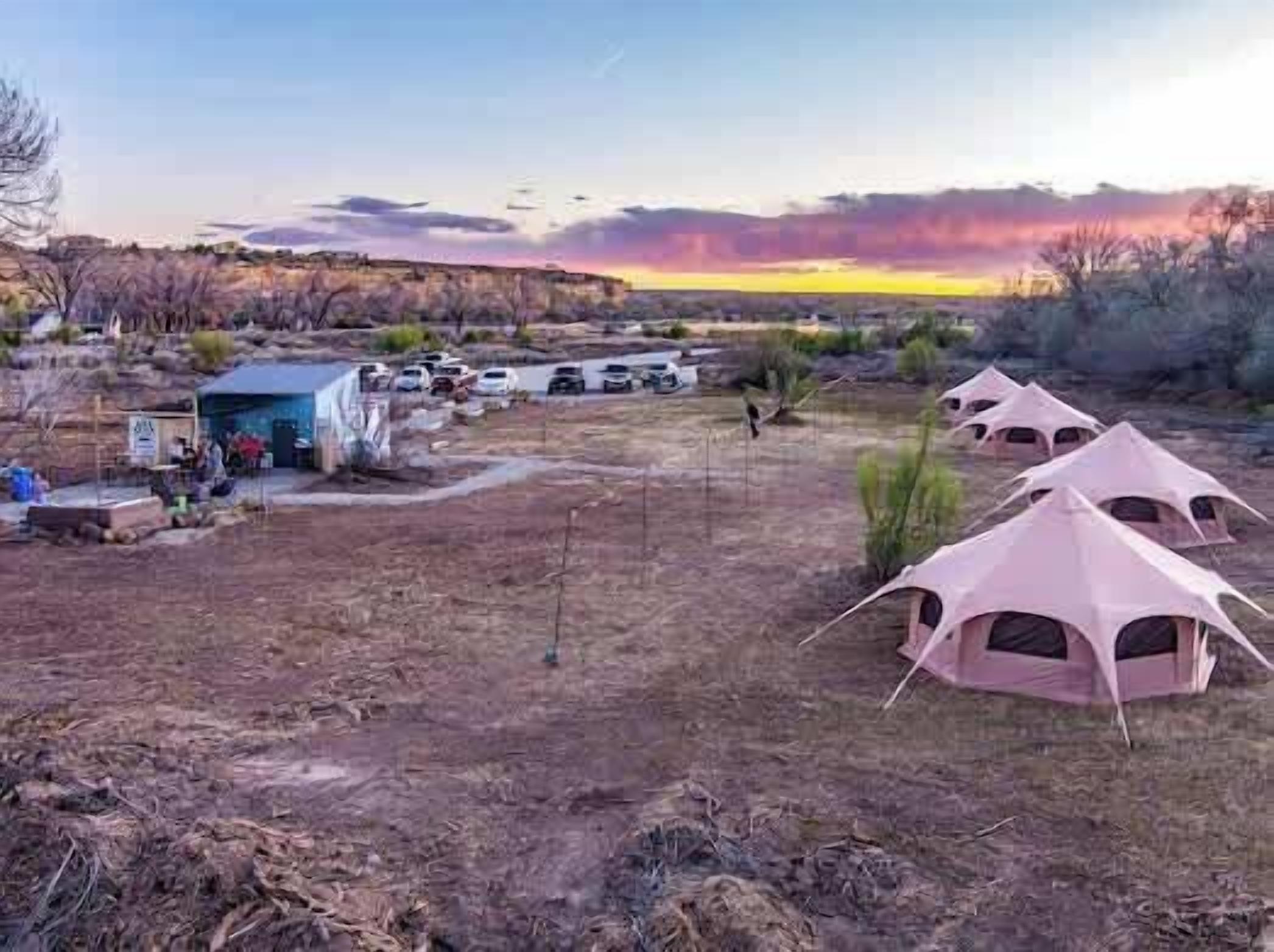 Un campamento con tiendas de campaña y un pequeño edificio, rodeado de terreno seco y vegetación escasa.