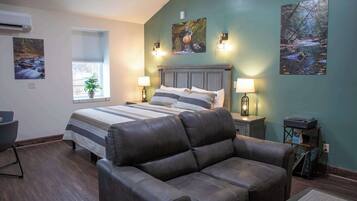 A bedroom with a bed, two bedside lamps, a window with blinds, a potted plant, and artwork on the walls.