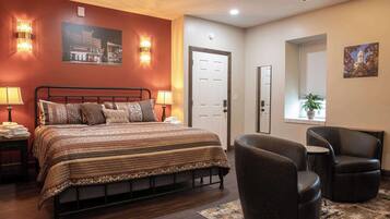 A bedroom with a bed, two bedside lamps, a door, a window with a plant, and a chair.
